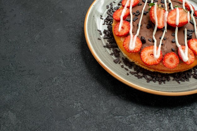 Vue rapprochée latérale du gâteau appétissant gâteau savoureux avec des morceaux de fraises et du chocolat sur une plaque blanche sur le côté droit du tableau noir