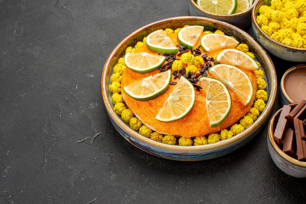 Vue rapprochée latérale du gâteau et du gâteau appétissant au chocolat et des bols de tranches de chocolat au citron vert et de crème au chocolat sur le tableau noir