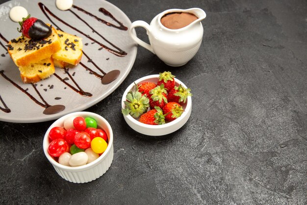 Vue rapprochée latérale du gâteau avec un gâteau au chocolat avec du chocolat et des fraises à côté des bols de fraises et de bonbons