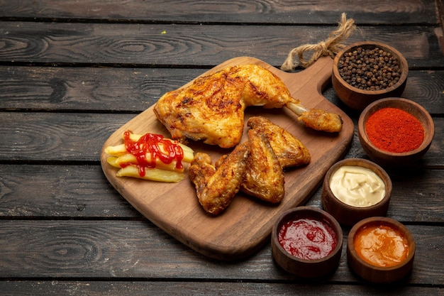 Vue rapprochée latérale du poulet cuisse et ailes de poulet appétissantes frites et bols de sauces colorées et d'épices sur la table