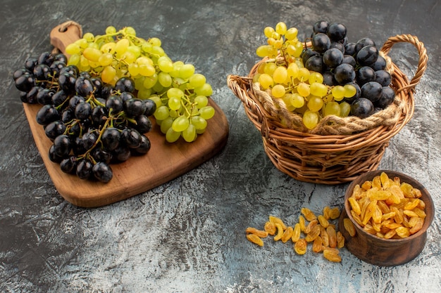 Vue rapprochée latérale des fruits le panier et la planche avec des raisins à côté du bol de fruits secs