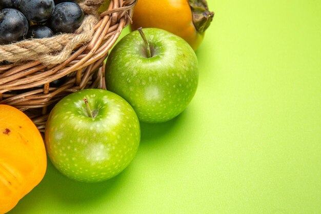 Vue rapprochée latérale fruits pommes vertes grappes de raisins noirs kakis sur la table verte