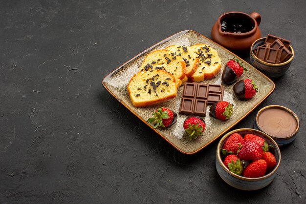 Vue rapprochée latérale gâteau aux fraises gâteau appétissant aux fraises enrobées de chocolat et bols de crème au chocolat fraise et chocolat sur le côté droit de la table