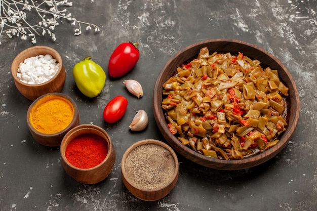 Photo gratuite vue rapprochée latérale plat appétissant plat appétissant de haricots verts à côté des bols d'épices colorées tomates ail et poivre sur la table sombre