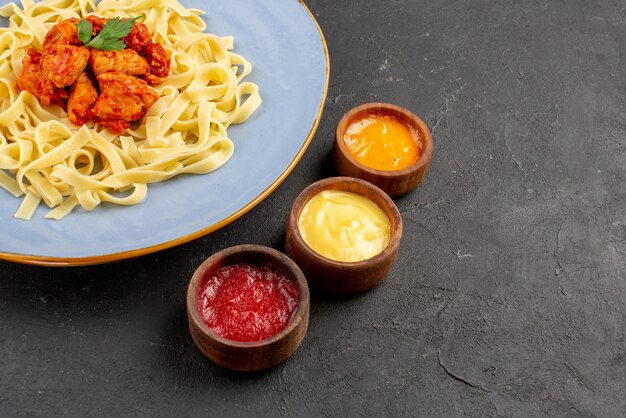 Vue rapprochée latérale plat appétissant plat de sauce pour pâtes et viande dans l'assiette bleue à côté des sauces colorées sur la surface sombre