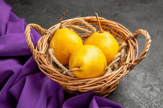 Vue rapprochée latérale des poires dans un panier panier en bois de poires jaunes sur la nappe violette sur la table sombre