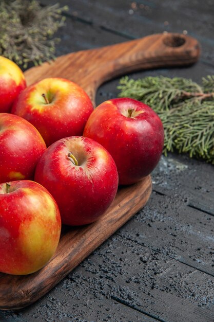 Vue rapprochée latérale des pommes et des branches des pommes jaune-rouge sur une planche à découper sur fond gris en bois entre les branches des arbres