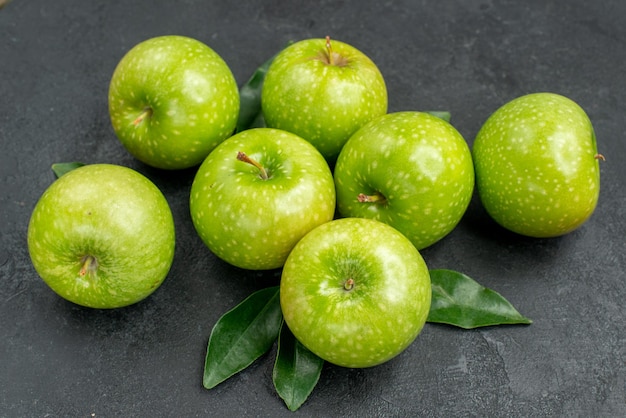 Vue rapprochée latérale des pommes sept pommes vertes appétissantes avec des feuilles sur la table