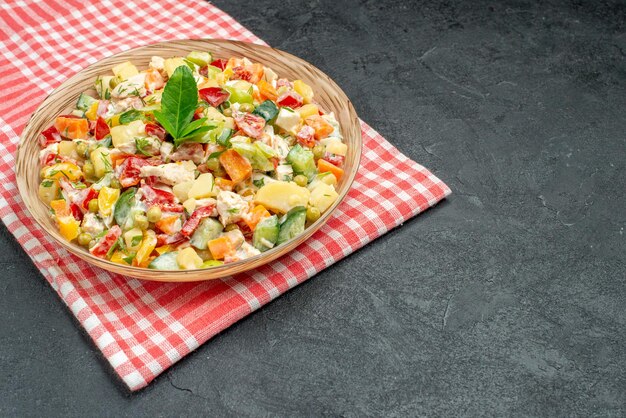 Vue rapprochée latérale de la salade de légumes dans un bol sur une serviette rouge sur fond gris foncé