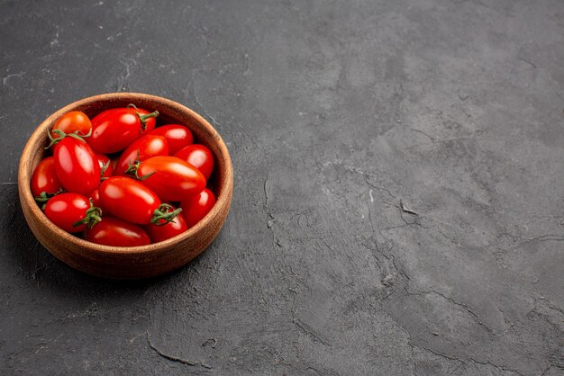 Vue rapprochée latérale des tomates bol en bois de tomates rouges mûres sur le côté gauche de la table sombre