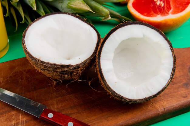 Vue rapprochée de la noix de coco coupée à moitié et un couteau sur une planche à découper avec d'autres agrumes sur fond vert