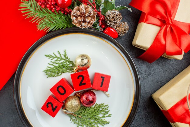 Vue rapprochée des numéros d'accessoires de décoration sur une assiette et de beaux cadeaux branches de sapin conifère sur une table sombre