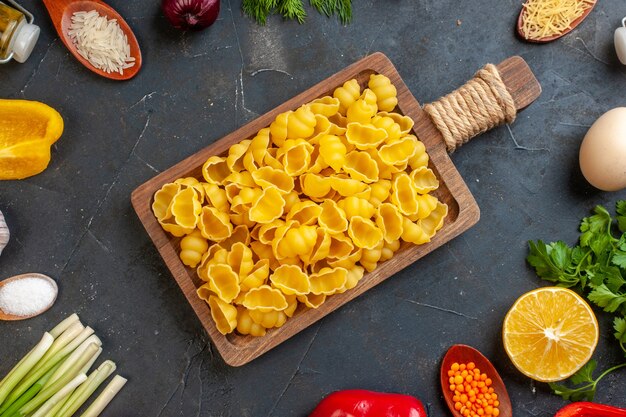 Vue rapprochée des pâtes crues dans une planche à découper brune oeufs légumes diverses épices sur dark