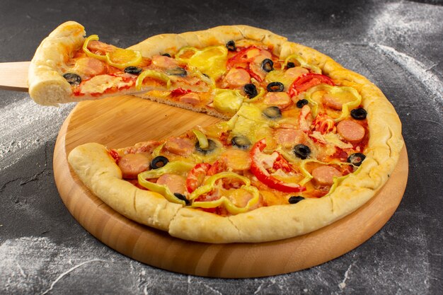 Vue rapprochée de la pizza au fromage avec tomates rouges, olives noires, poivrons et saucisses sur la surface sombre