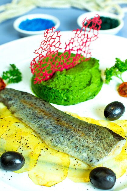 Photo gratuite vue rapprochée de poisson cuit à la vapeur avec du brocoli en purée et des pommes de terre en tranches et des olives noires sur une plaque blanche sur bleu