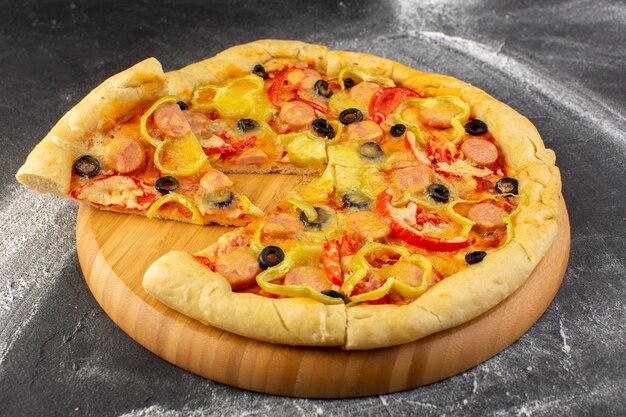 Vue rapprochée de la savoureuse pizza au fromage avec tomates rouges, olives noires, poivrons et saucisses sur le bureau sombre