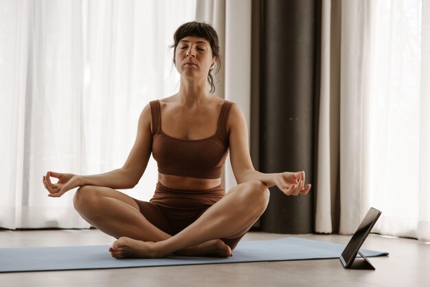 Vue rapprochée des sportives faisant du yoga sur un ordinateur portable avec les yeux fermés