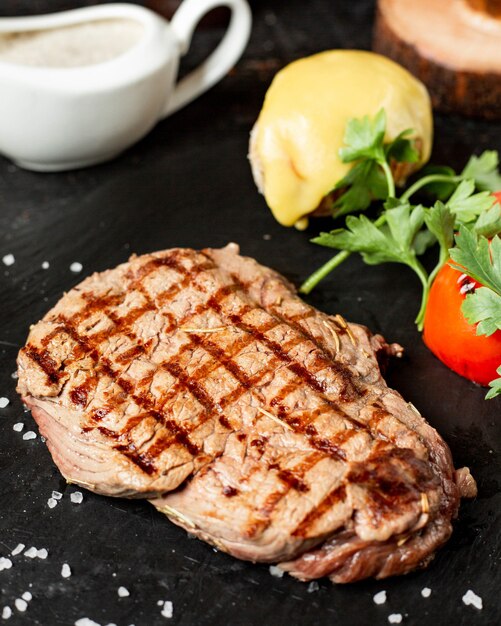 Vue rapprochée de steak de boeuf grillé servi avec des légumes persil et sauce sur tableau noir