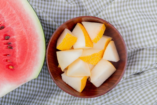 Photo gratuite vue rapprochée de tranches de melon dans un bol avec la moitié de la pastèque sur fond de tissu à carreaux