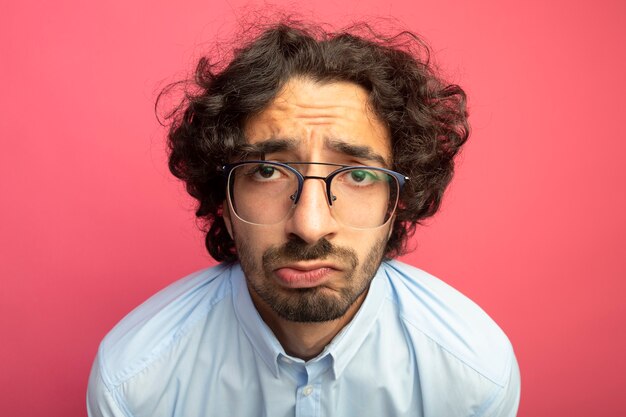 Vue rapprochée de triste jeune bel homme caucasien portant des lunettes isolé sur mur cramoisi