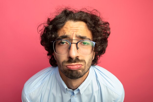 Vue rapprochée de triste jeune bel homme portant des lunettes regardant avant isolé sur mur rose