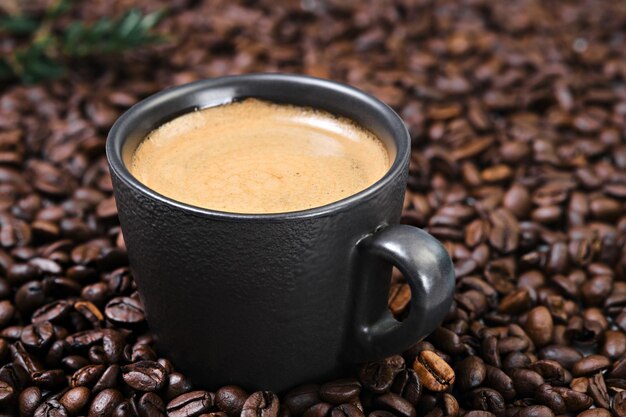 Vue réaliste du café expresso noir dans la tasse sombre dans les grains de café torréfiés. Tasse avec de la crème de café et des grains de café. Gros plan et mise au point sélective sur la tasse