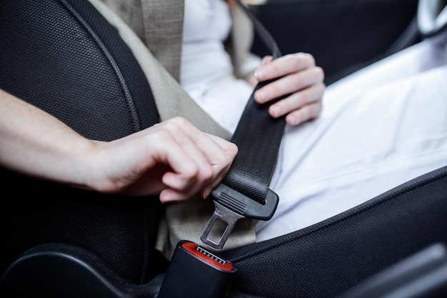 Vue recadrée de la femme attachant la ceinture de sécurité assise dans la voiture au premier plan flou Vue en coupe des mains de la jeune femme verrouillant la ceinture de sécurité dans la voiture Assis seul Gros plan