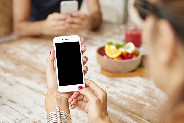 Vue recadrée des mains féminines avec manucure rouge tenant un téléphone portable avec écran blanc.