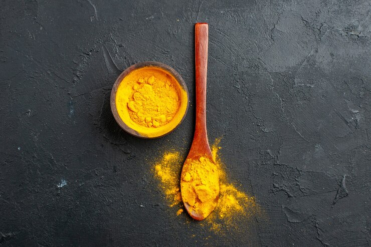 Photo gratuit vue supérieure du bol de curcuma, du curcuma dans une cuillère en bois sur une table sombre, espace libre