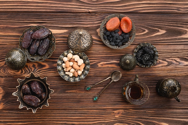 Photo gratuite une vue surélevée de dattes fraîches du ramadan; des noisettes; fruits secs et thé sur un bureau en bois