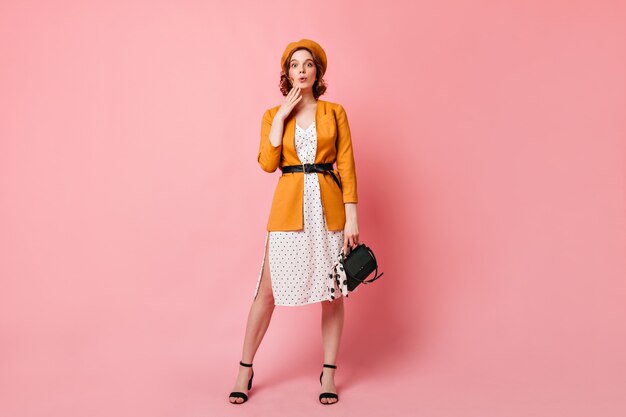 Vue sur toute la longueur de la dame française jocund avec sac à main. Photo de Studio de fille mince à la mode en béret jaune.