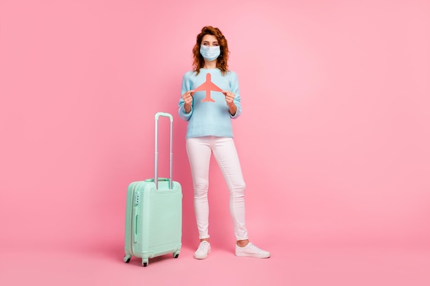 Vue sur toute la longueur d'une fille tenant dans les mains un avion en papier portant des voies respiratoires isolées sur fond de couleur pastel rose