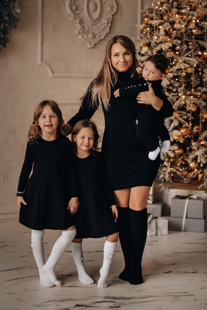 Vue sur toute la longueur de l'heureuse mère avec ses petits enfants debout ensemble près de l'arbre de Noël à la maison. Concept de joyeuses fêtes