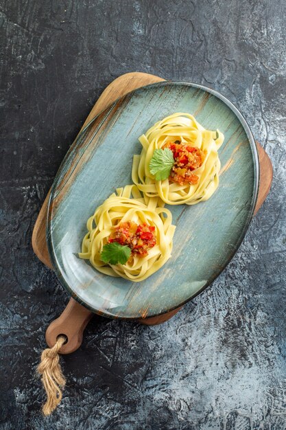 Vue verticale d'une assiette bleue avec un délicieux repas de pâtes servi avec de la tomate et de la viande sur une planche à découper sur une table sombre