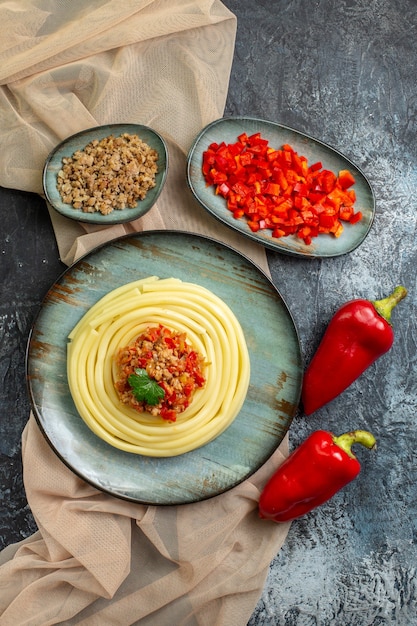 Vue verticale d'une assiette bleue avec un délicieux repas de pâtes servi avec de la tomate et de la viande sur une serviette de couleur beige hachée et des poivrons entiers