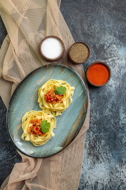 Vue verticale d'une assiette bleue avec un délicieux repas de pâtes servi avec de la tomate et de la viande sur une serviette de couleur beige pour le dîner différentes épices
