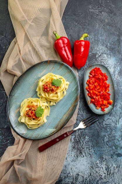 Vue verticale d'une assiette bleue avec un délicieux repas de pâtes servi avec de la tomate et de la viande sur une serviette de couleur beige pour le dîner ses ingrédients