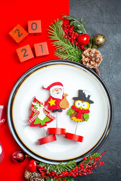 Vue verticale de l'assiette à dîner accessoires de décoration branches de sapin et numéros chaussette de Noël sur une serviette rouge sur une table noire