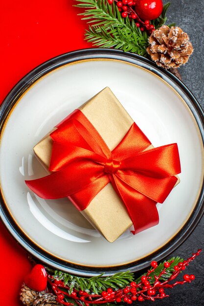 Vue verticale des assiettes avec cadeau sur elle et branches de sapin avec cône de conifère accessoire de décoration sur une serviette rouge