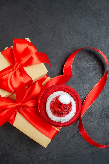 Vue verticale de beaux cadeaux avec ruban rouge et chapeau de père Noël sur table sombre