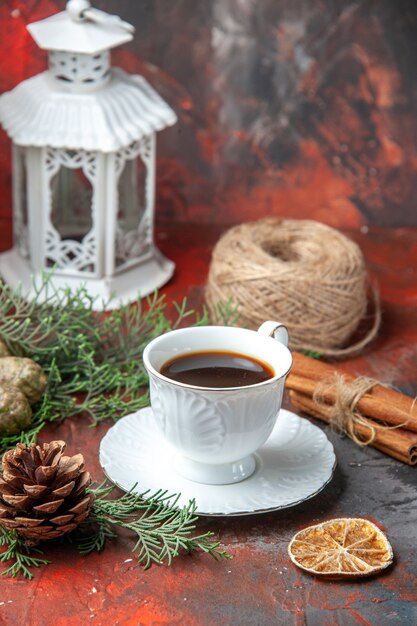 Vue verticale des branches de sapin citron vert cannelle cône de conifère une boule de corde une tasse de thé noir sur fond rouge