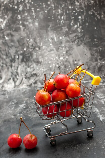 Vue verticale des cerises rouges à l'intérieur et à l'extérieur du mini-tableau commercial avec sur gris