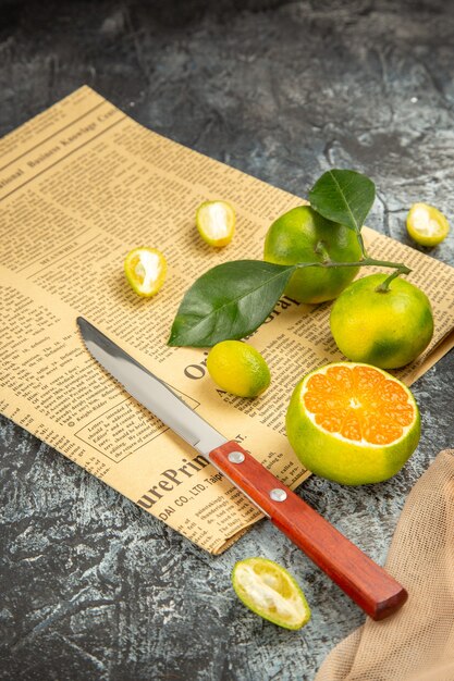 Vue verticale de citrons frais dans un panier noir tombé sur un couteau à serviette et un journal sur une table grise