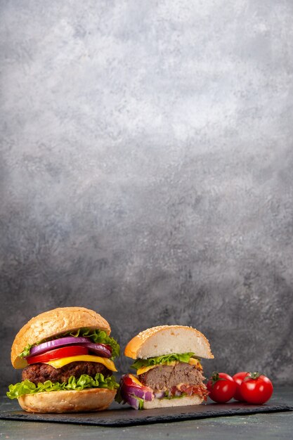 Vue verticale de la coupe entière divers sandwichs savoureux et tomates avec tige sur plateau noir sur surface floue grise