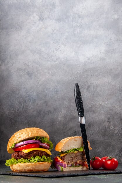 Vue verticale de la coupe entière de savoureux sandwichs et tomates avec couteau à tige sur plateau noir sur une surface de couleur sombre mix