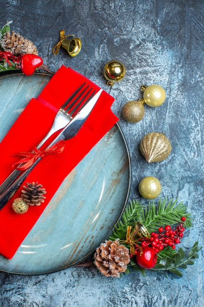 Vue verticale de couverts avec ruban rouge sur une serviette décorative sur une assiette bleue et accessoires de Noël sur fond sombre