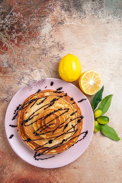 Vue verticale de crêpes étouffantes décorées de sirop de chocolat et de citron sur table colorée