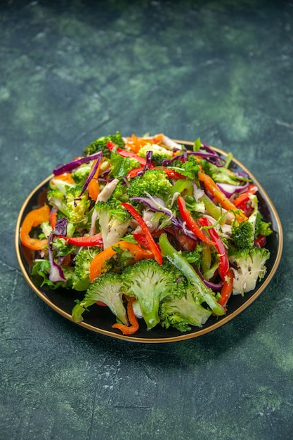 Photo gratuite vue verticale d'une délicieuse salade végétalienne dans une assiette avec divers légumes frais sur fond sombre