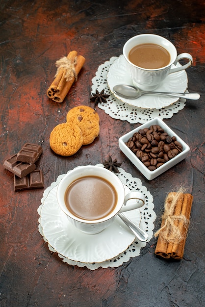 Vue verticale d'un délicieux café dans des tasses blanches sur des serviettes, des biscuits, des barres de chocolat à la cannelle et au citron vert sur fond de couleur mélangée