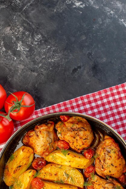 Vue verticale d'un délicieux dîner avec des poulets verts de pommes de terre dans une casserole sur une serviette dénudée rouge pliée tomates fraîches sur fond de couleur sombre